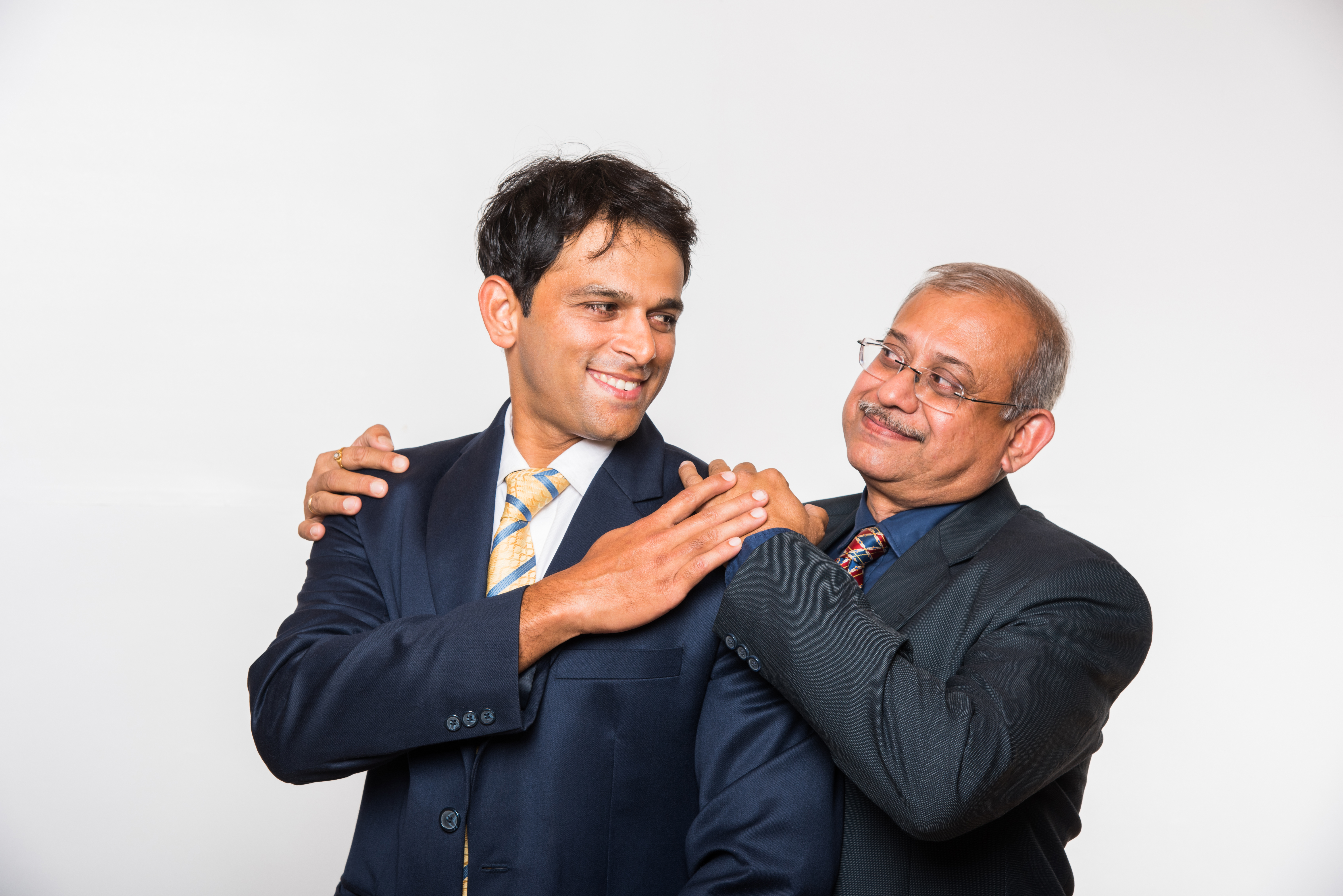2 men, brown-skin, one youngish, one oldish, it appears, in suits, next to each other close, older one has arm around other and hand on shoulder, and other has hand on other's hand on shoulder