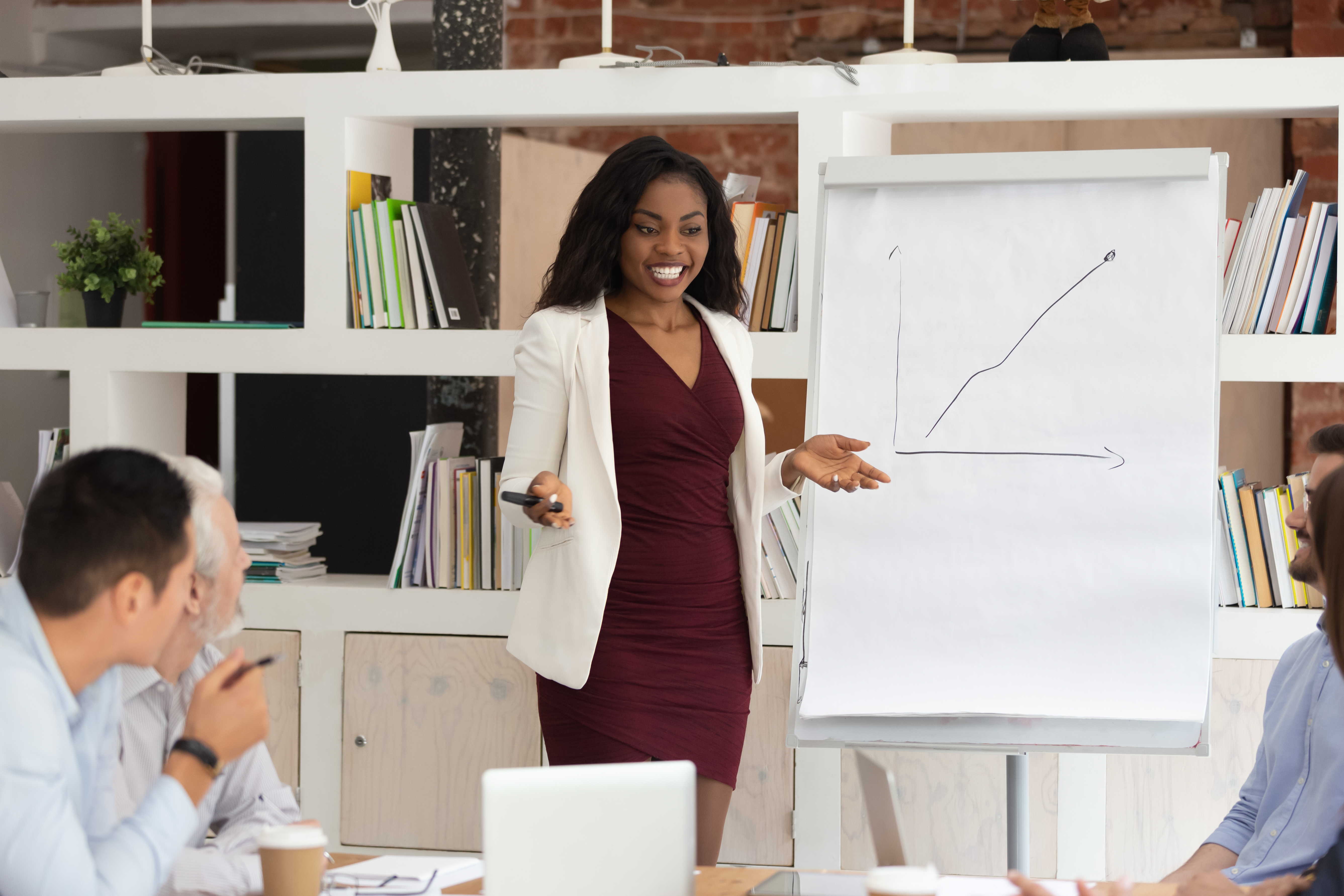 An African American woman presenting a graph amongst others in a meeting. 