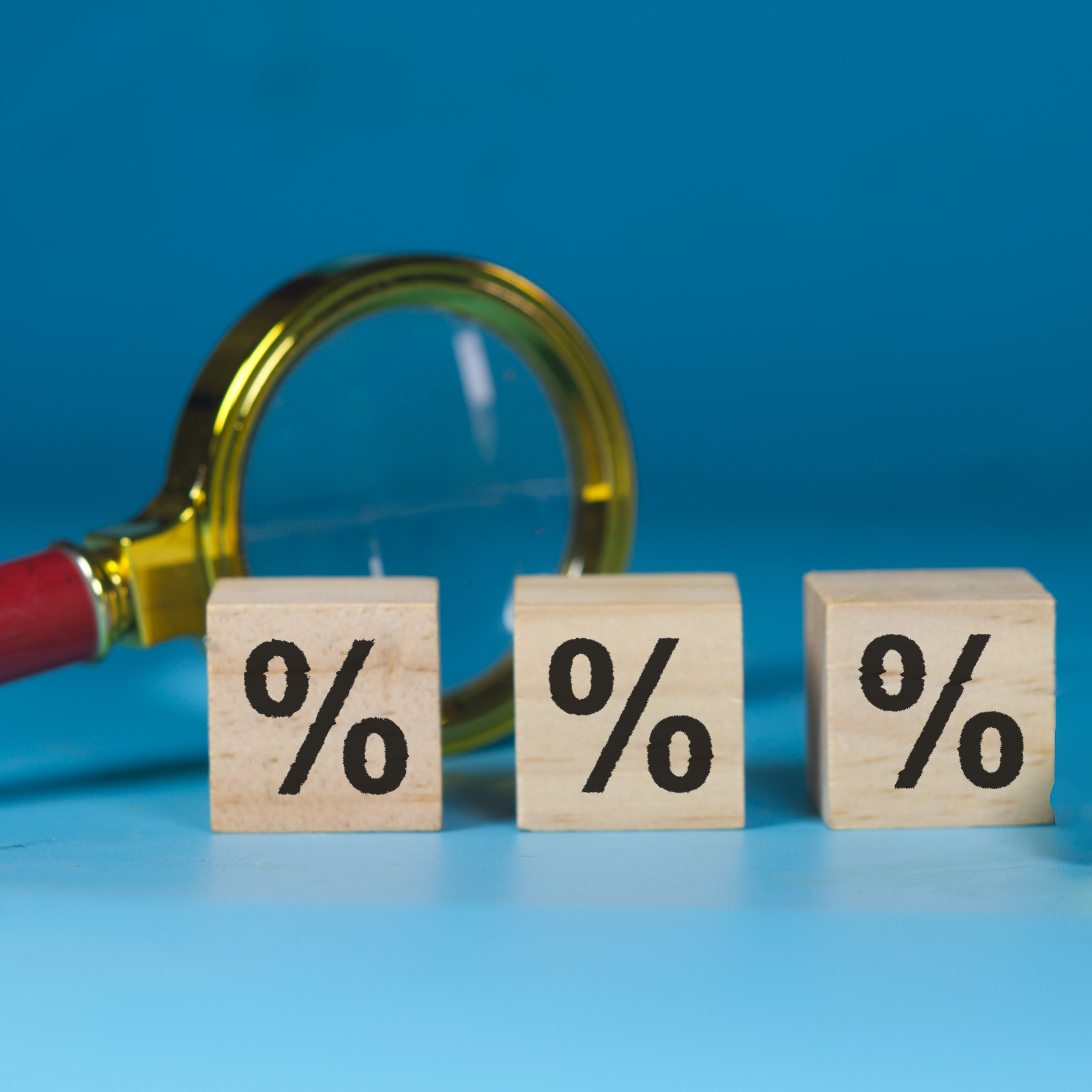 Wooden cubes with percent signs on them, magnifying glass in the background
