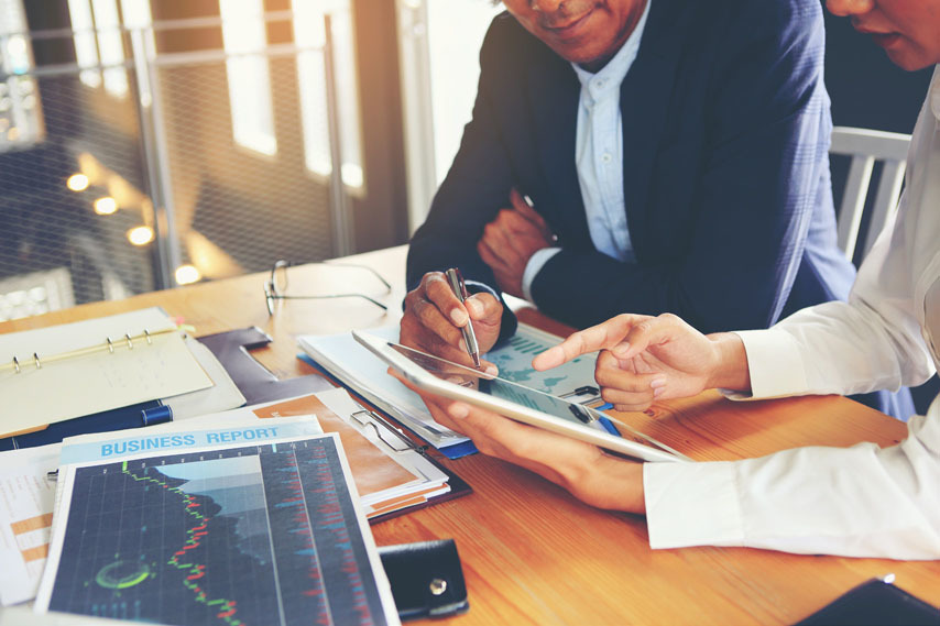 Business people discussing what is on an iPad. Sitting at a table with several files and papers.