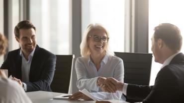 Smiling woman and man at boardroom table shaking hands 