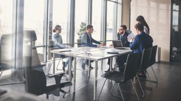 five professionals seated at a table in a meeting