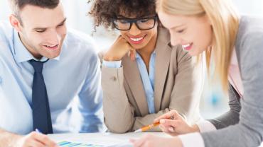 three professionals leaning on a table reviewing papers