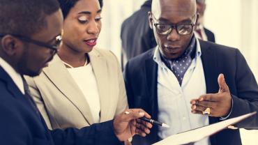 three standing professionals review a document together