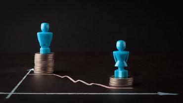 a male token atop a stack of quarters and a downtrend chart (left to right) with a female token atop a smaller stack of quarters