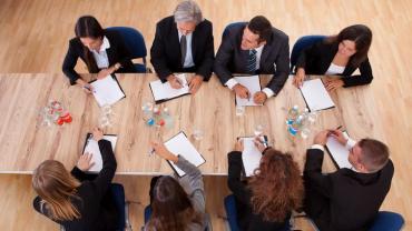 eight business people seated around a square table; 4 on each side