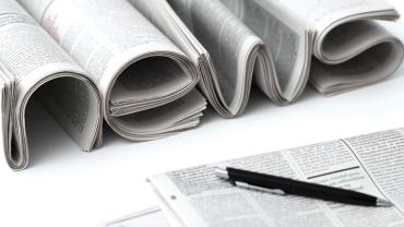 multiple newspapers and a pen on a table