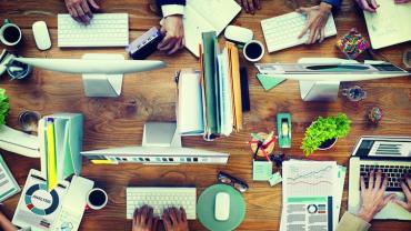 top view of a desk with four users working on computers and papers organized next to them