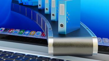 Blue binders on conveyor belt moving from inside a computer screen onto a keyboard.