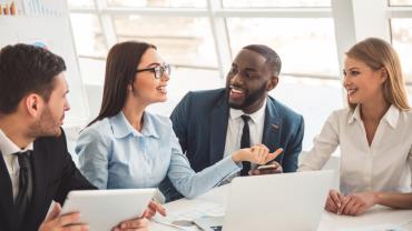 Group of diverse business professionals smiling and chatting in a sunny meeting room.