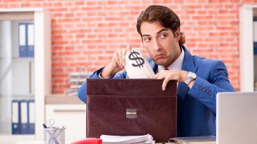 man, looks like, white or brown skin, stealing bag with dollar sign into portfolio case, wearing suit, in office setting