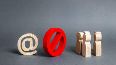 illustration or photo of what appears to be wood figures - on the left an at (@) sign, in the middle the universal sign for something being prohibited, a red circle with a slash inside, and to the right, figures representing people 