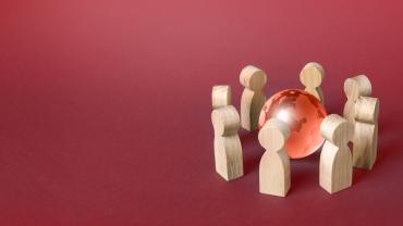 Wooden humanoid figures gathered around a small globe. 