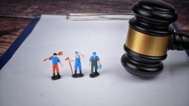 Three miniature toy workers on a clipboard next to a gavel.  