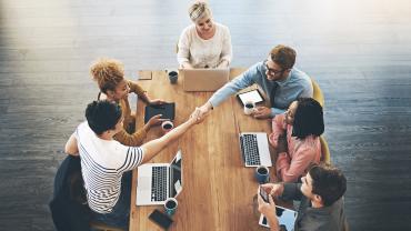 Workers shake hands across a table