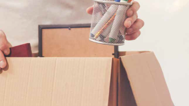 a hand putting a cup of pens in a cardboard box