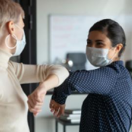 elbow bumping -- looks like 2 women, one white, one brown-skinned