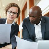 a female professional holding papers reviews documents with a male professional
