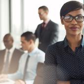 professional female in glasses in the foreground with three colleagues faded in the background