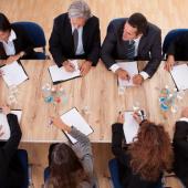 eight business people seated around a square table; 4 on each side