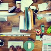 top view of a desk with four users working on computers and papers organized next to them