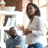 young black woman stands and speaks to a room of diverse colleagues