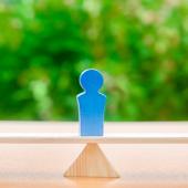 Three wooden figures balancing on a beam in front of greenery.