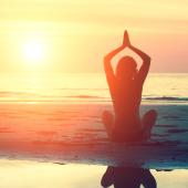 Silhouette of woman doing yoga on the beach during sunrise.