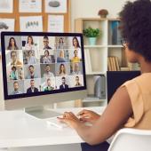 Black woman, appears to be, at desk with array of people on screen, far off but appears to be different skin colors
