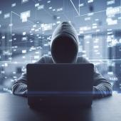 Figure in gray hoodie on a computer with data in the background. 