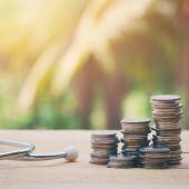 Close up of a stethoscope and stack of coins on an old wood table. 
