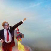 man, it appears, white, suited, propelled by jet engines, hand thrust toward sky