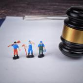 Three miniature toy workers on a clipboard next to a gavel.  