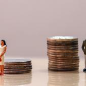 Figurine of woman with a stack of coins smaller than the one of the man next to her. 