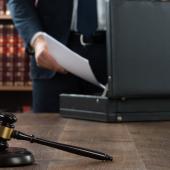 a person in a suit putting papers in a briefcase. a gavel is in the foreground