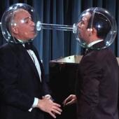 two men with plastic globes over their heads. they are facing one another and the globes are connected with a tube