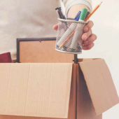a hand putting a cup of pens in a cardboard box