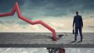 Red line chart plummeting into sidewalk next to a businessman in front of a cloudy gray sky.